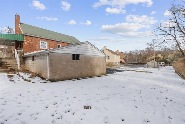 snow covered property with concrete block siding, fence, a storage unit, and an outdoor structure