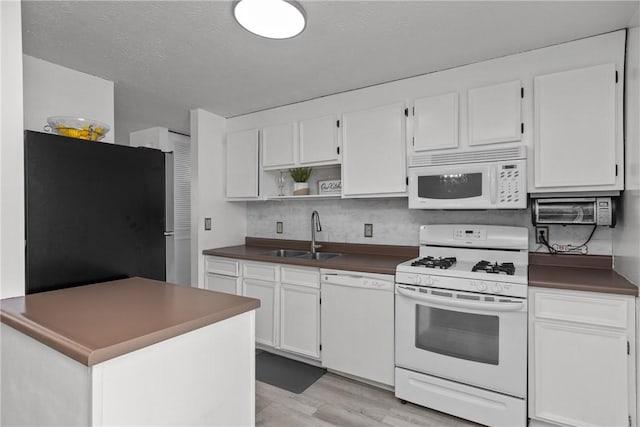 kitchen with dark countertops, white appliances, white cabinetry, and a sink