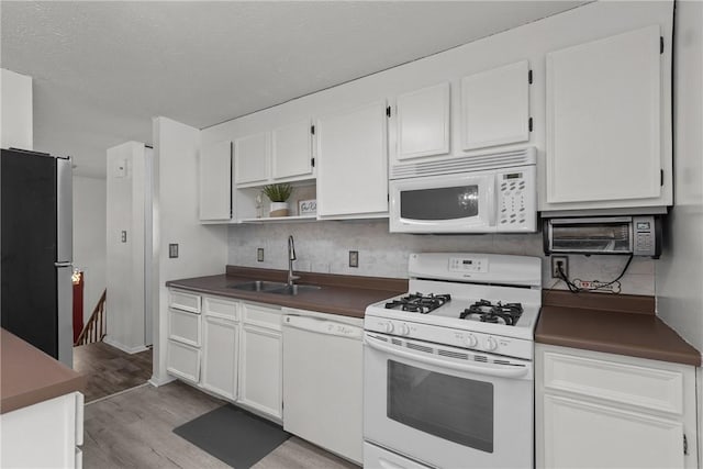 kitchen with dark countertops, white appliances, white cabinetry, and a sink