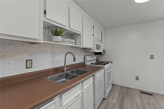 kitchen with dark countertops, white appliances, white cabinets, and a sink