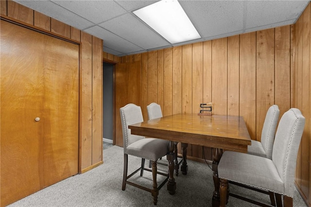 dining space with light carpet, wood walls, and a paneled ceiling