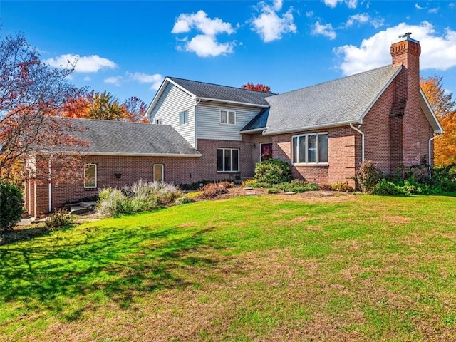 rear view of property featuring a yard, brick siding, a chimney, and roof with shingles