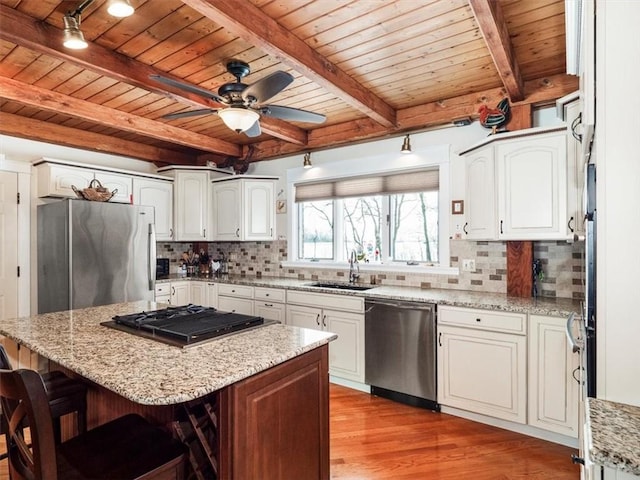 kitchen with tasteful backsplash, appliances with stainless steel finishes, a sink, and light stone countertops