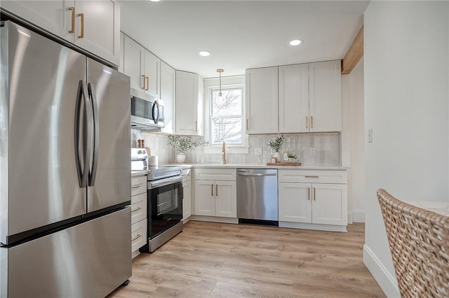 kitchen featuring stainless steel appliances, light countertops, decorative light fixtures, and white cabinetry