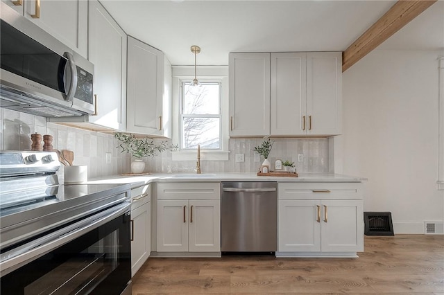 kitchen featuring white cabinets, appliances with stainless steel finishes, light countertops, pendant lighting, and a sink