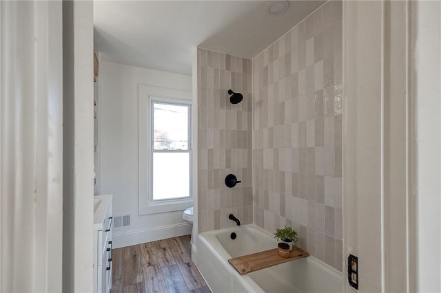 full bathroom with toilet, wood finished floors, visible vents, baseboards, and washtub / shower combination