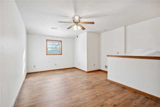 empty room featuring light wood-type flooring, ceiling fan, visible vents, and baseboards