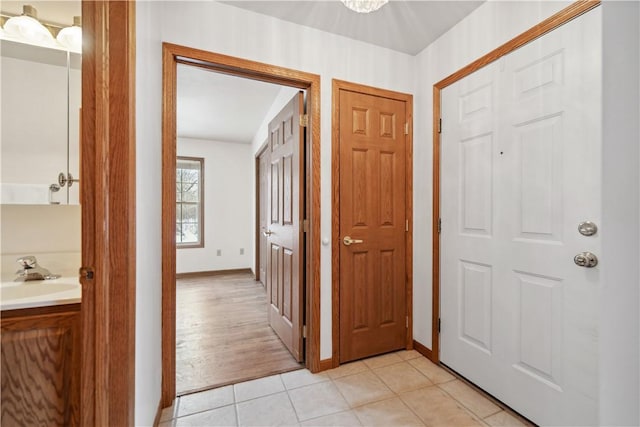 corridor featuring light tile patterned floors, baseboards, and a sink