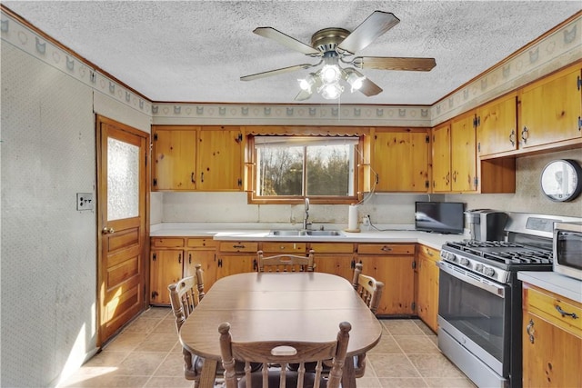 kitchen with brown cabinets, light countertops, a textured ceiling, stainless steel range with gas cooktop, and a sink