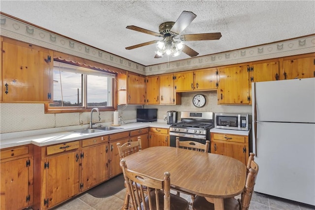 kitchen with a textured ceiling, a sink, light countertops, appliances with stainless steel finishes, and brown cabinets