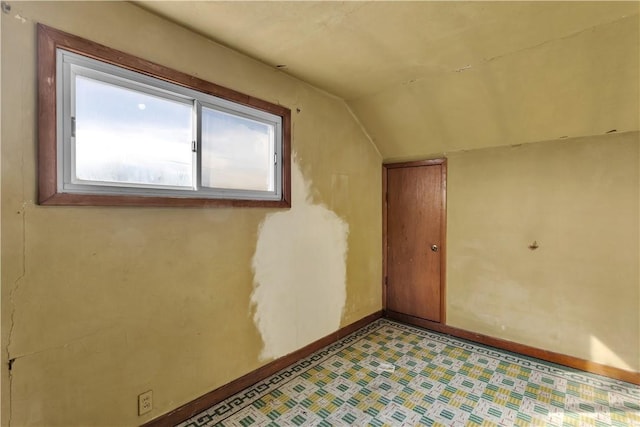 empty room featuring lofted ceiling, light floors, and baseboards