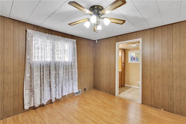 unfurnished room with a wealth of natural light, ceiling fan, wood walls, and wood finished floors