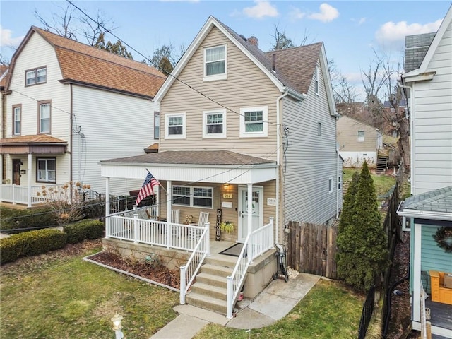 view of front of house with covered porch, roof with shingles, a front yard, and fence