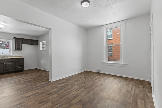 unfurnished room with baseboards, visible vents, dark wood-type flooring, a textured ceiling, and a sink