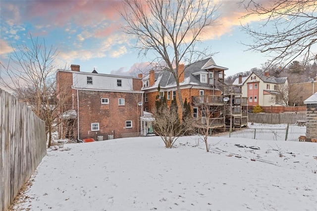 snow covered rear of property featuring a chimney, fence, and brick siding