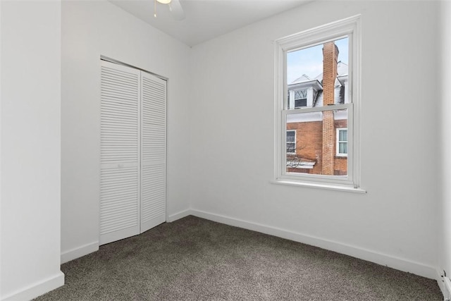 unfurnished bedroom with ceiling fan, dark colored carpet, a closet, and baseboards