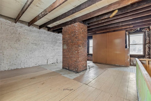 interior space featuring light wood finished floors, brick wall, and beam ceiling