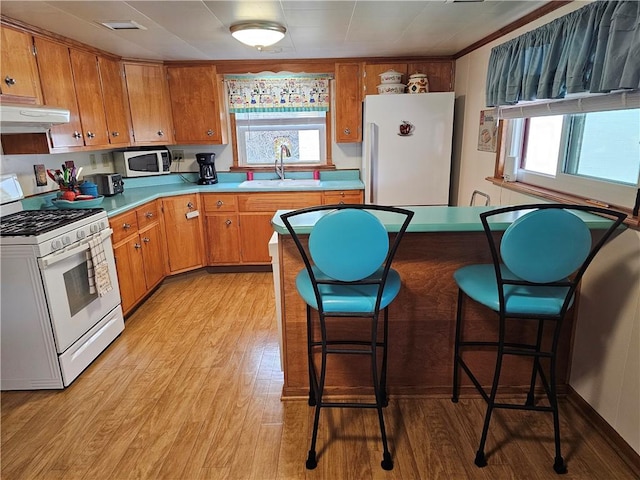 kitchen featuring brown cabinets, white appliances, light countertops, and a sink