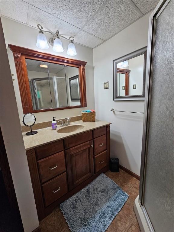 full bath with tile patterned flooring, a paneled ceiling, vanity, baseboards, and a shower stall