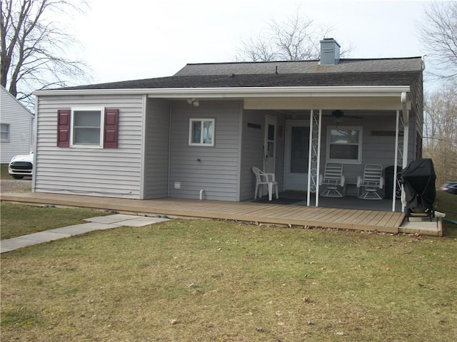 rear view of property with roof with shingles, a yard, a chimney, and a wooden deck