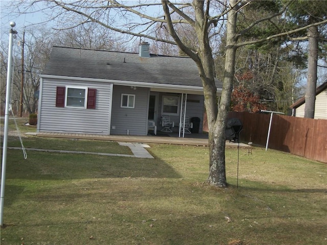 exterior space with a shingled roof, a lawn, a chimney, and fence