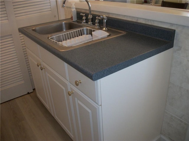 room details featuring wood finished floors, dark countertops, a sink, and white cabinetry