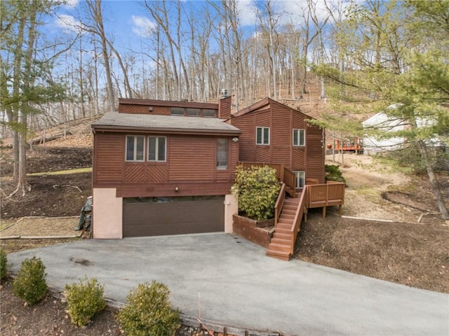 view of front of home with driveway, an attached garage, stairs, a wooden deck, and stucco siding