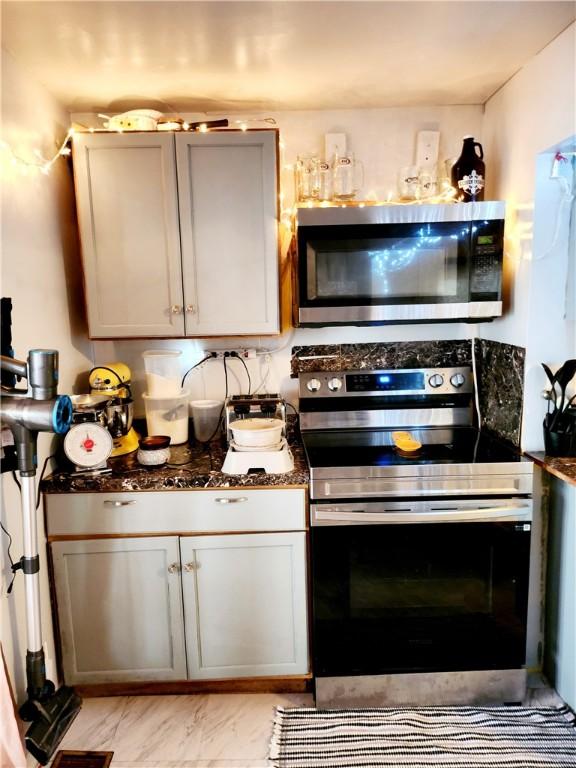 kitchen with dark stone counters, stainless steel appliances, marble finish floor, and gray cabinetry