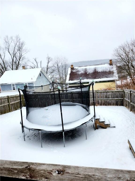 snow covered deck with a fenced backyard and a trampoline