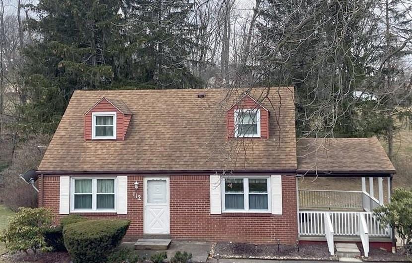 new england style home featuring roof with shingles, a porch, and brick siding