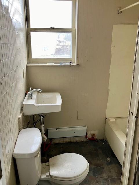 full bathroom featuring a bathtub, tile walls, toilet, baseboard heating, and a sink