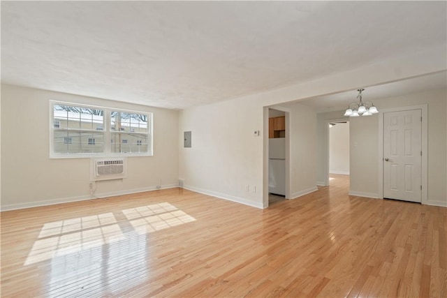 empty room with electric panel, baseboards, light wood-style floors, a chandelier, and a wall mounted AC