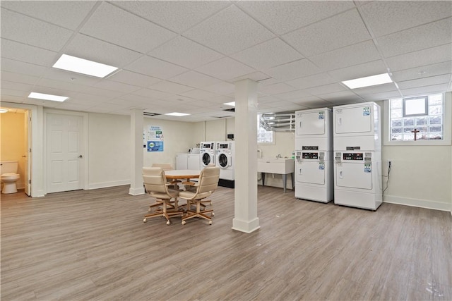 basement with baseboards, a paneled ceiling, stacked washer and clothes dryer, light wood-type flooring, and a sink