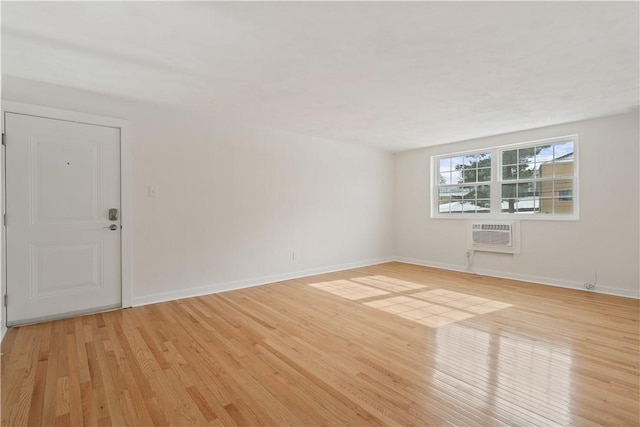 spare room with light wood-style floors, baseboards, and a wall mounted air conditioner