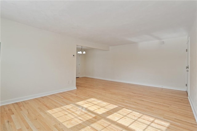 empty room featuring baseboards, light wood finished floors, and an inviting chandelier