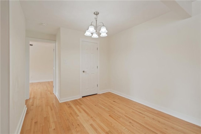 empty room with an inviting chandelier, wood finished floors, and baseboards