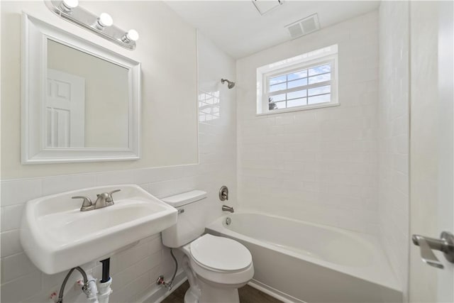 bathroom featuring visible vents, wainscoting, toilet, tile walls, and shower / bathing tub combination