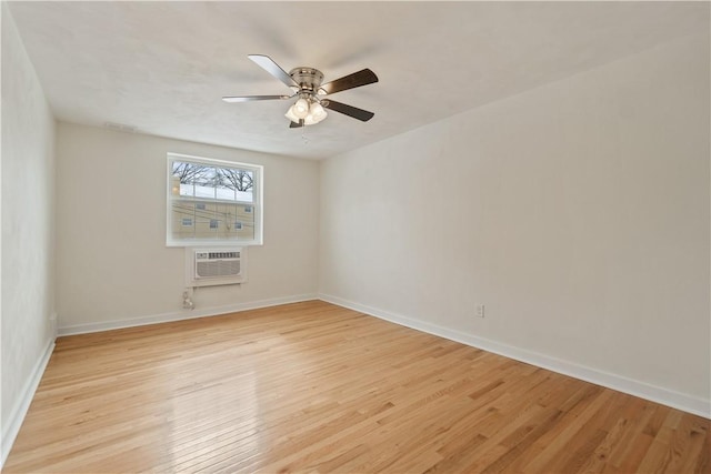 spare room featuring an AC wall unit, light wood finished floors, a ceiling fan, and baseboards