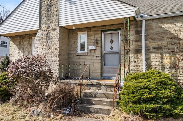 doorway to property with a shingled roof and stone siding