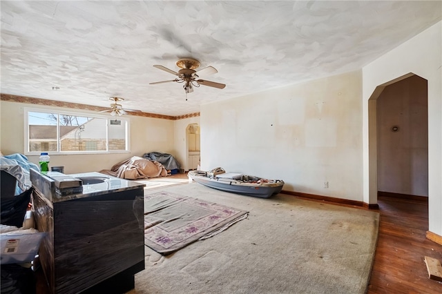 interior space featuring arched walkways, dark wood-style flooring, a ceiling fan, a textured ceiling, and baseboards