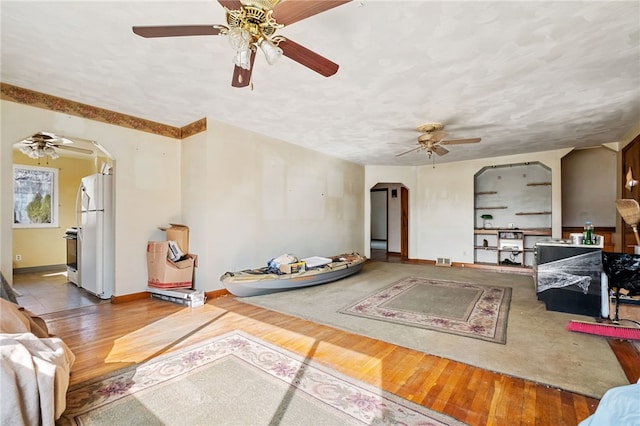 living area featuring arched walkways, wood finished floors, visible vents, a ceiling fan, and baseboards