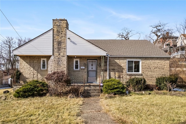 view of front facade with a shingled roof, a front yard, and a chimney