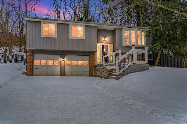 bi-level home featuring a garage, brick siding, and fence