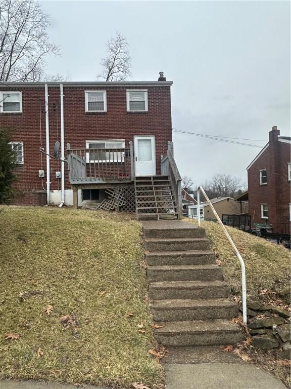 view of front of home featuring brick siding, a chimney, a wooden deck, a front lawn, and stairs