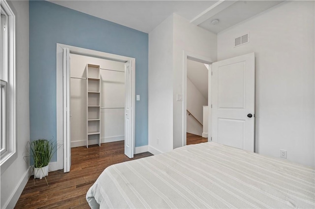 bedroom with baseboards, visible vents, dark wood-style flooring, a walk in closet, and a closet