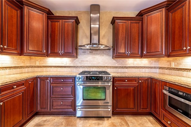 kitchen featuring reddish brown cabinets, light stone counters, tasteful backsplash, stainless steel gas range oven, and wall chimney exhaust hood