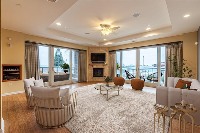 living room featuring baseboards, a glass covered fireplace, wood finished floors, a tray ceiling, and french doors