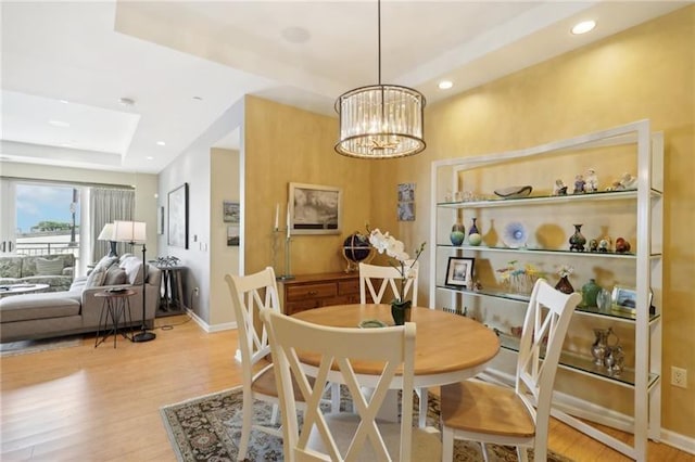 dining space with recessed lighting, baseboards, a tray ceiling, light wood finished floors, and an inviting chandelier