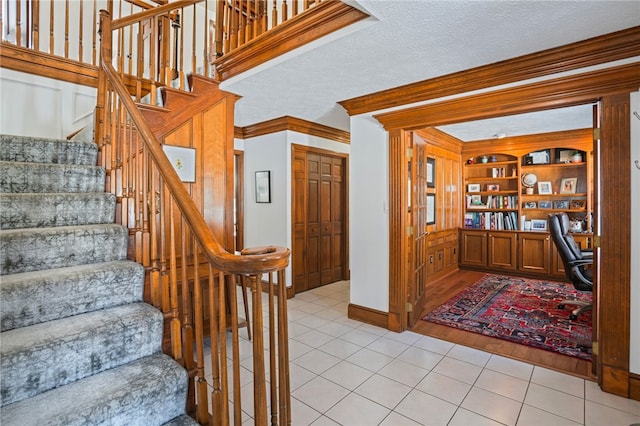 stairs with built in features, built in study area, ornamental molding, tile patterned flooring, and a textured ceiling