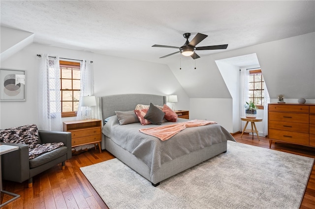 bedroom featuring dark wood-style floors, lofted ceiling, multiple windows, and a ceiling fan